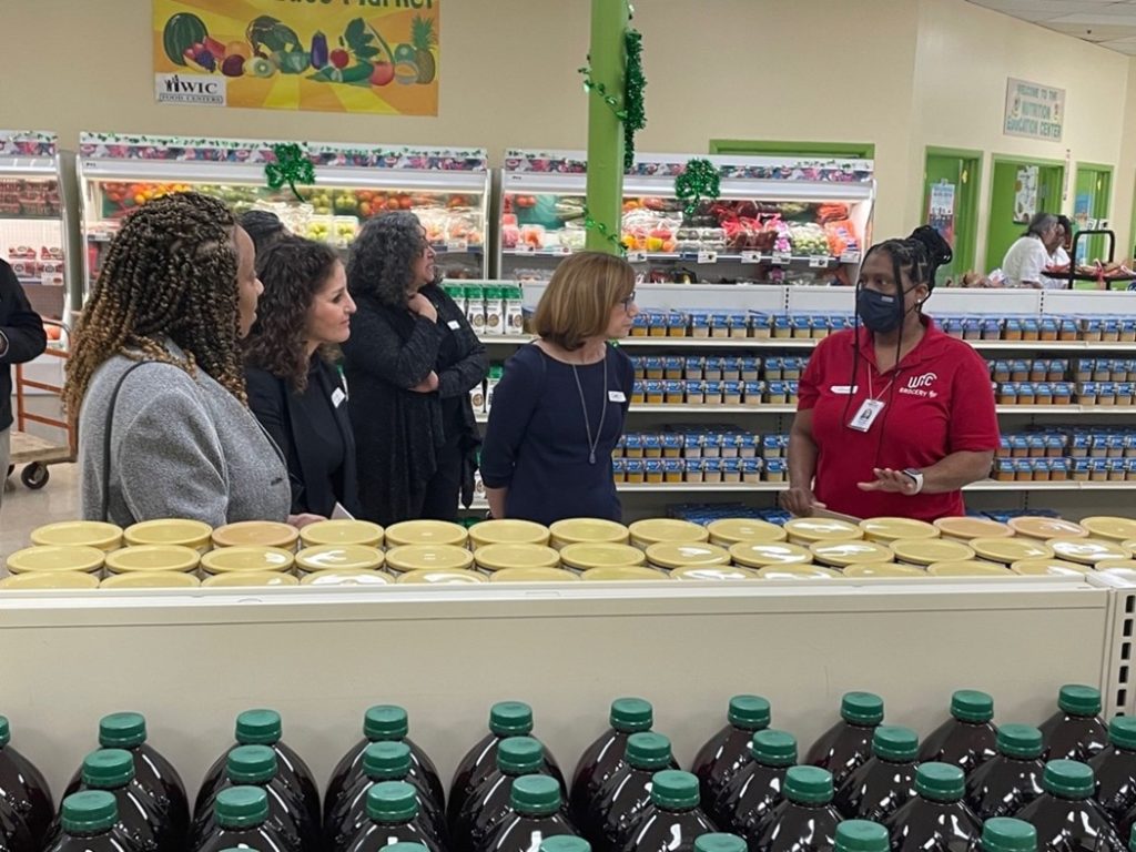 WIC Center Director, Tiffany Gilder (red polo), speaks with Administrator Long and others about the Catholic Charities WIC center products and services. February 2023