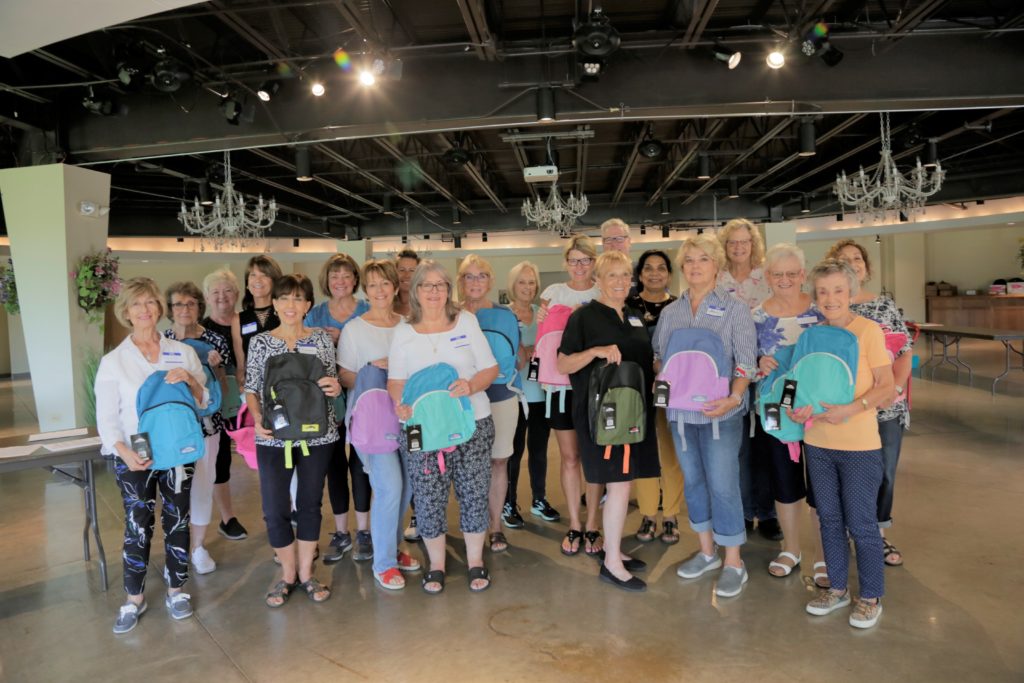 Group of people smiling and holding backpacks.