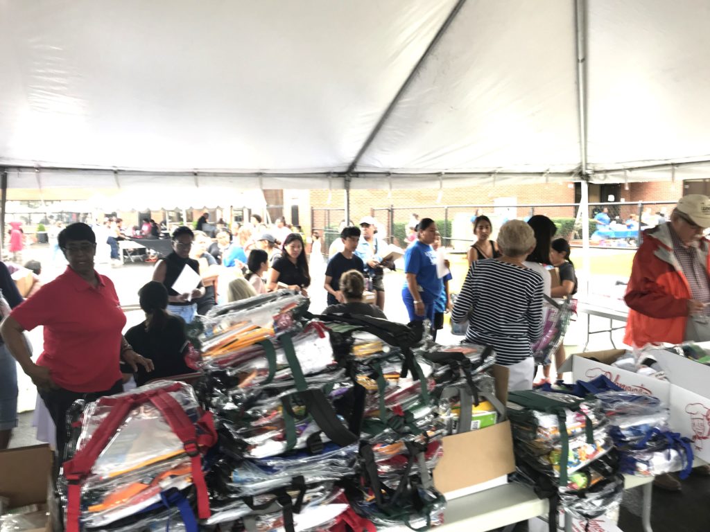 A large group of people walking around tents with backpacks on tables.