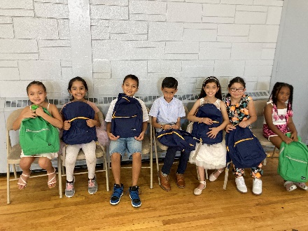 Group of children sitting and smiling with backpacks.