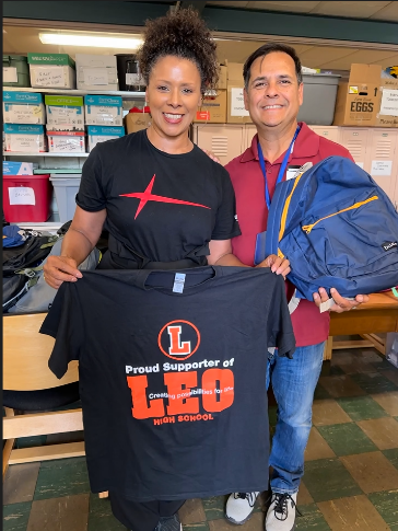 Two people standing and smiling; one is holding t-shirt that says Proud Support of LEO High School