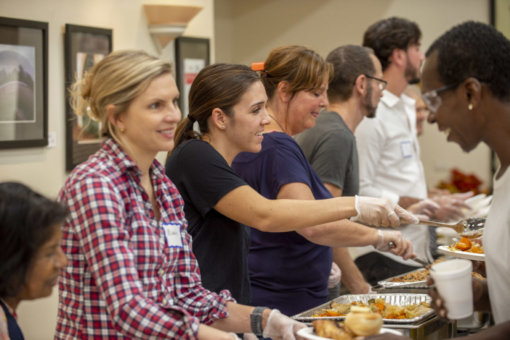 People smiling and serving food across a long table