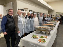 Group of people lined up with aprons standing by catered meal.