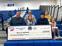 Shawn H. and family sitting on bleachers and holding a large gift check for $5,000.