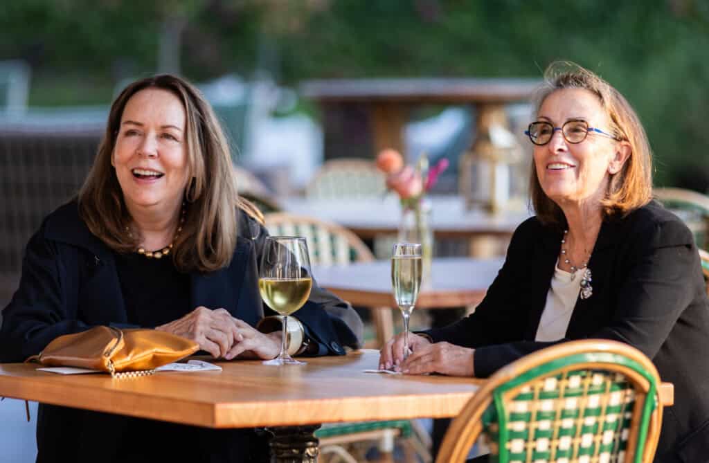 Two women smiling with drinks at the Art of Caring fundraiser